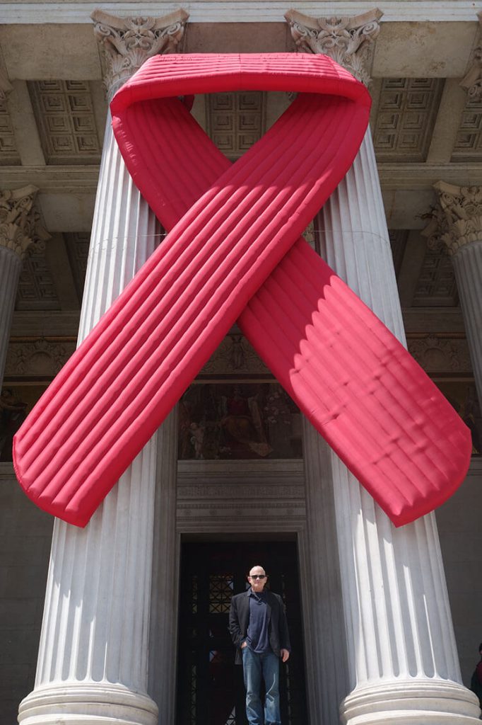 Bill Roedy standing beneath a large AIDS awareness ribbon